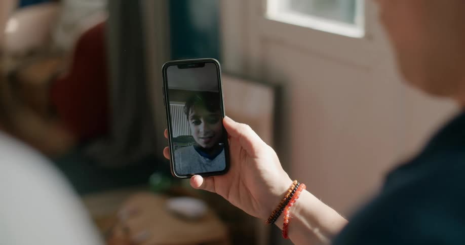 Two people sit at home and watch a child on a cell phone