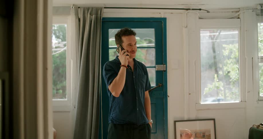 A man talks on the phone while standing near the front door of his house