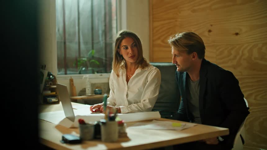 A man and woman sit together at an office desk with a laptop