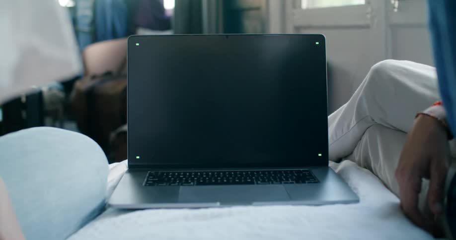 A person in a room sitting on a couch next to a laptop with a door in the background