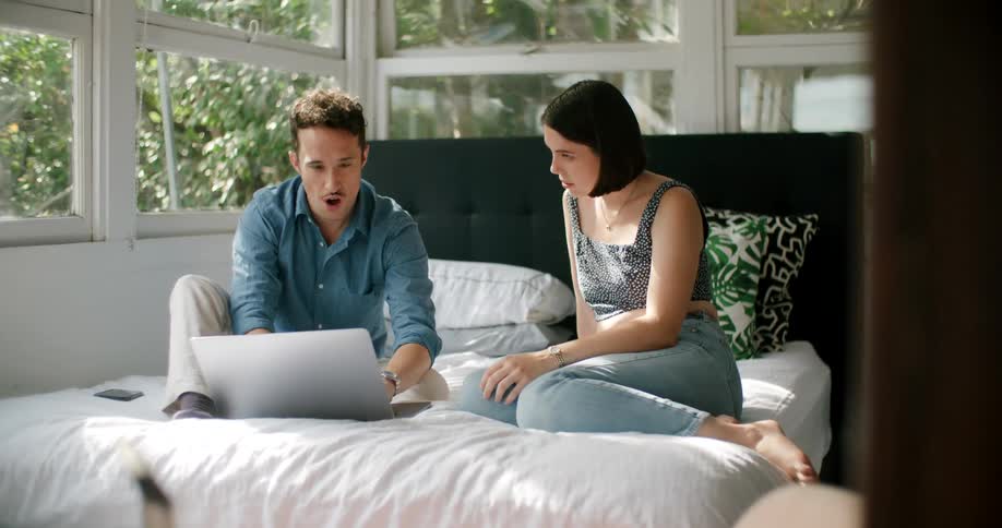 Young couple sitting in bed at home with a laptop having a conversation