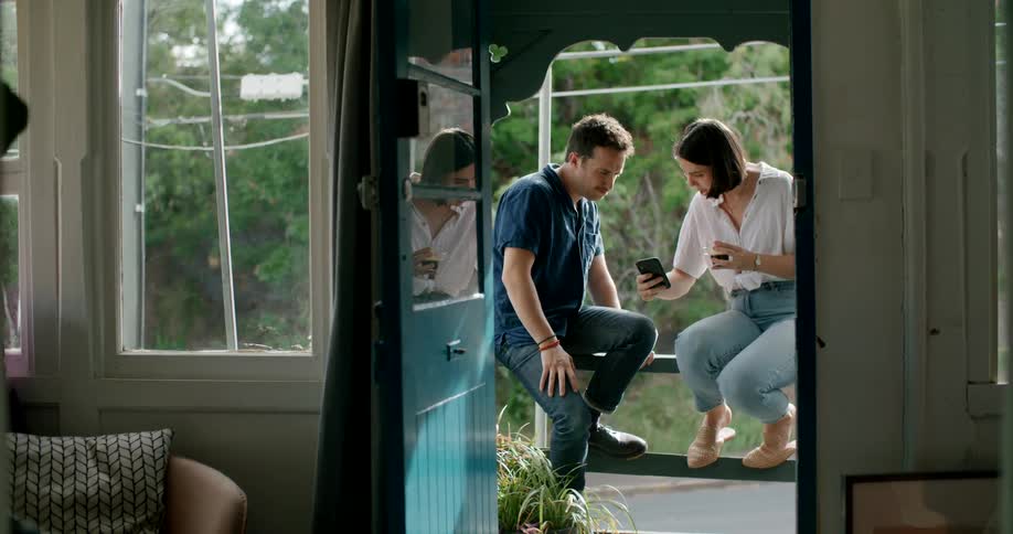 A man and woman sitting on a patio talking looking at a phone
