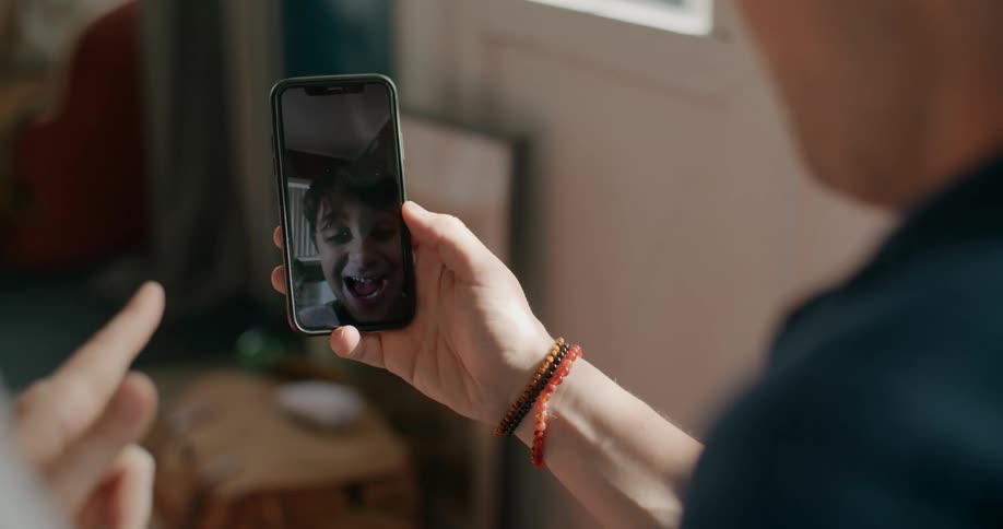 Two people sit at home and watch a child on a cell phone