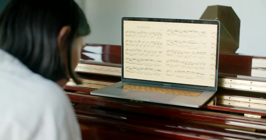 A woman using a laptop with sheet music showing to play the piano
