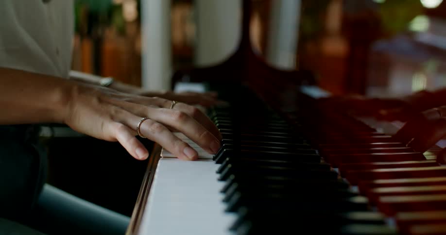 A female pianist plays a large piano indoors during the day