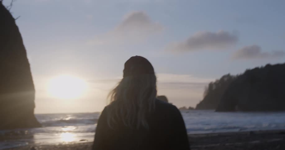 A woman is walking towards the water of a beach at sunset