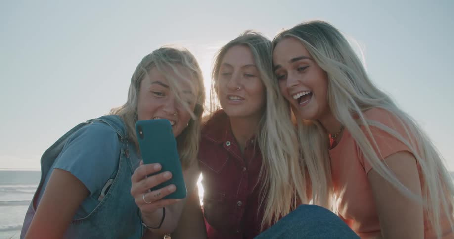 A group of women at a beach looking at a cell phone