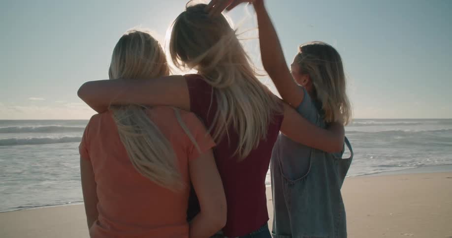 Three young female friends hugging in front of the sea at sunset