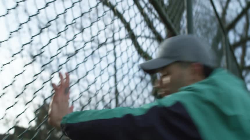 A man forcefully pushes himself against a chain link fence in a park