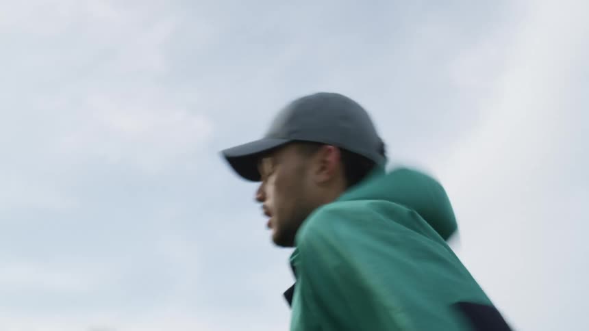 Young man jogging on the green grass on a field in a park near town