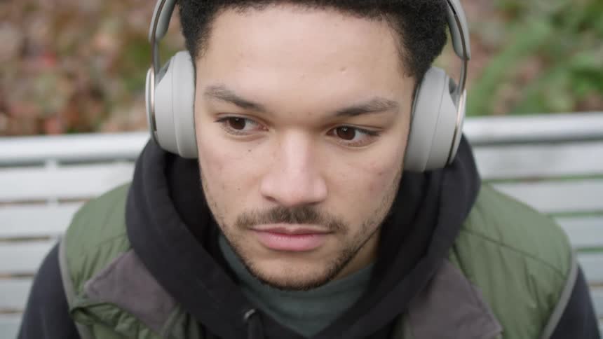 A man puts on headphones as he sits on a bench outside
