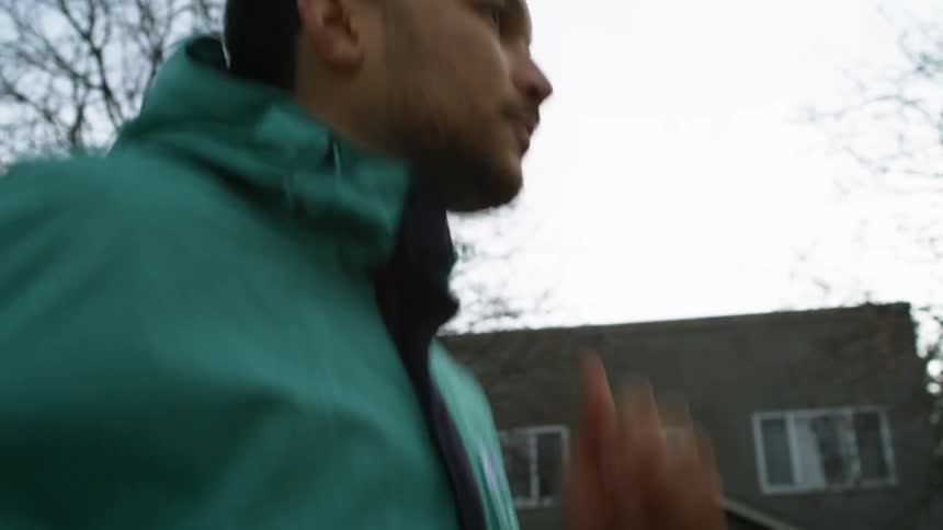 A man wears a green windbreaker as he jogs past homes in a neighborhood