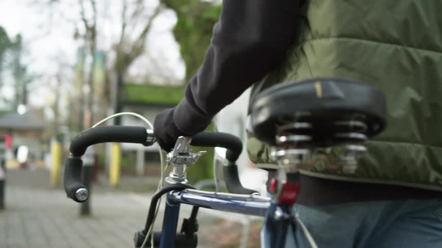 A man walks his bicycle down a cobblestone sidewalk through a quaint neighborhood