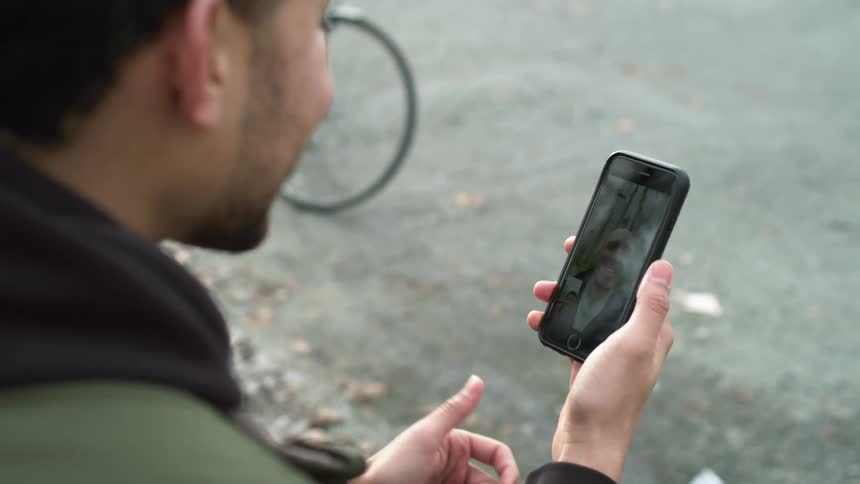 A man sits outside and video chats on a cell phone with another man