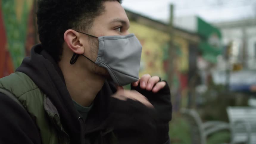 A man sitting outside puts a mask on