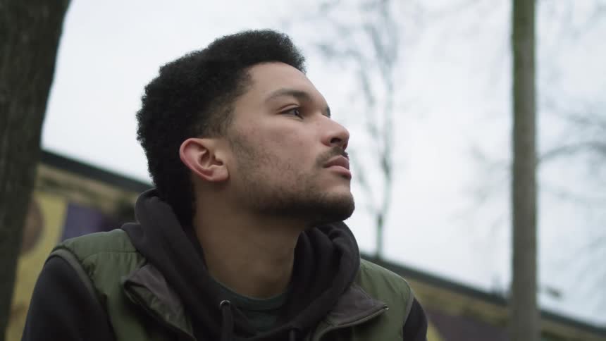 A young man sits outside and watches a bird fly over a house