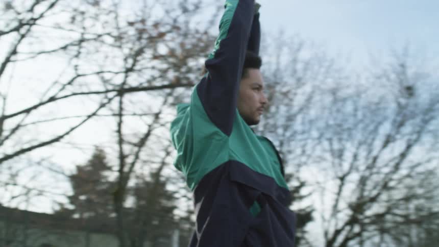 Young man stretching on the green grass of a soccer field in a small town at morning
