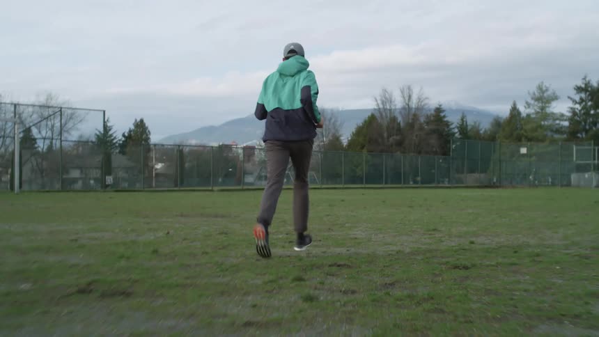 Man jogging over the green grass in a field on a public park near a town