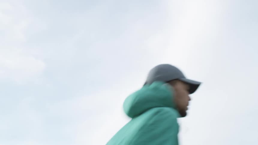 A man in a jacket jogs through a field on a cloudy day