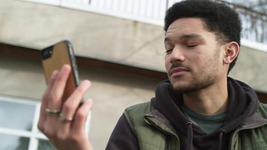 Young man answering a video call on his phone smiles while talking outdoors