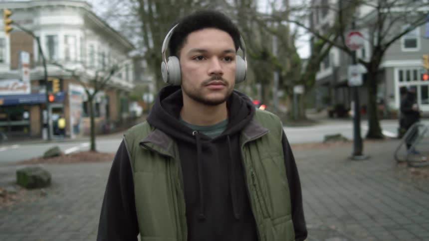 Young man wearing headphones walks down a boulevard on the streets of a town