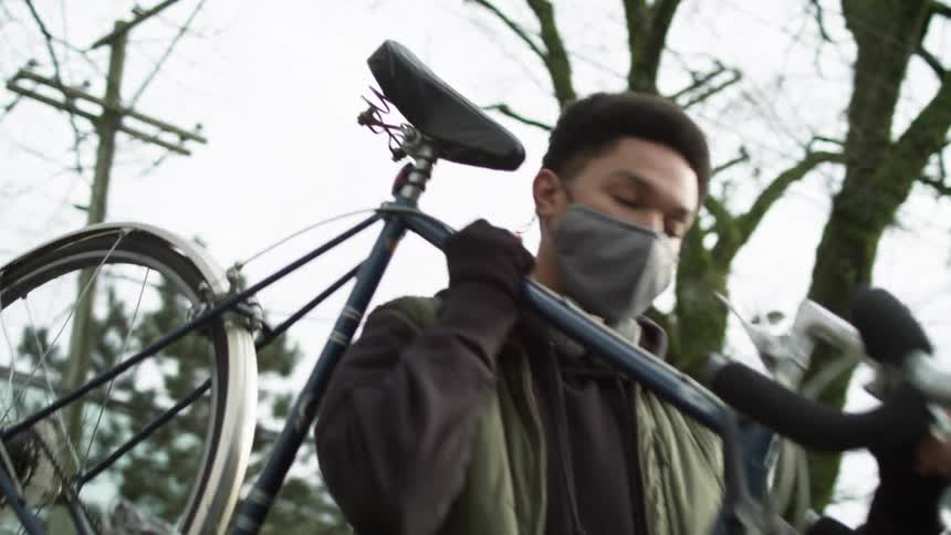 Young man wearing a face mask walking on the neighborhood picks up a bicycle