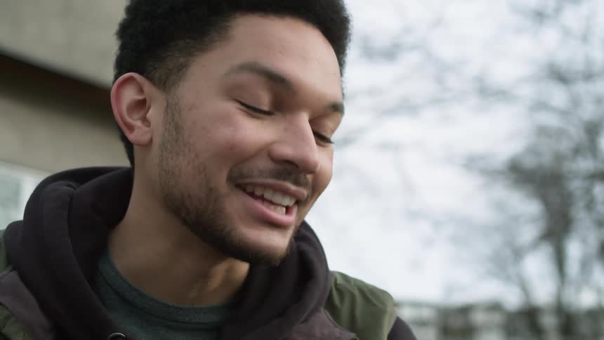 A man laughs while on a video call on his smartphone in a park