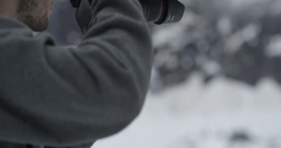 A man aims a camera and takes a picture on a snowy day