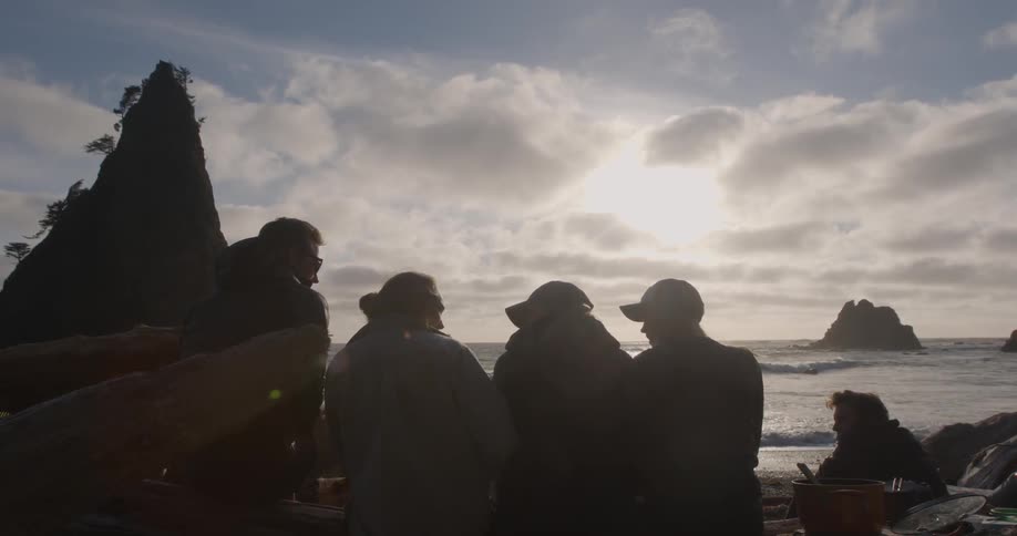 A group of people sit on the beach and look towards the ocean on a cloudy day