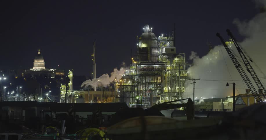 Smoke billows from an oil refinery in a city at night