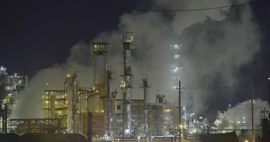 Smoke billows from a large refinery at night