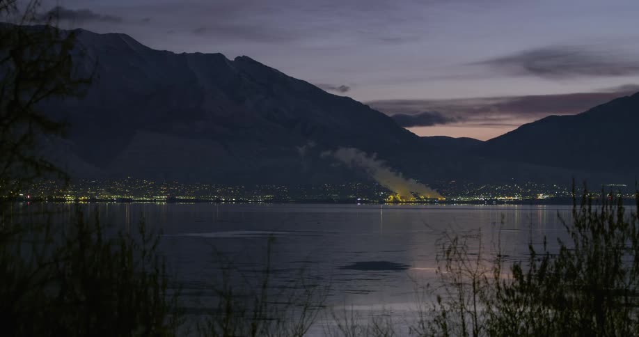 A city below a mountain range and across a large lake is lit up at night
