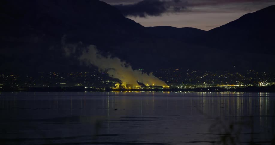 A power plant that has steam coming off of it near a lake