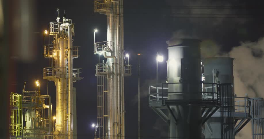 Smoke and flame rising from a large oil refinery at night