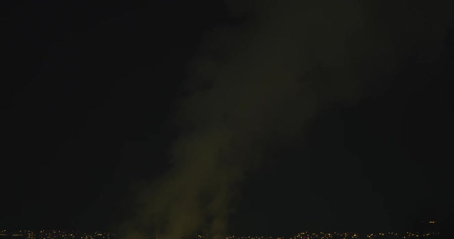Smoke rising from a large factory into a black night sky