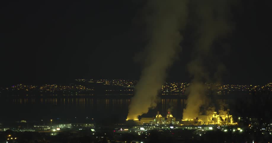 Clouds of steam rising from a power plant in a small town near a lake at night