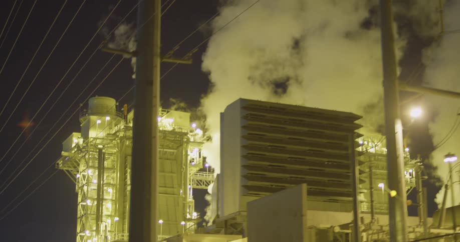 A power plant at night with steam and lights with power lines