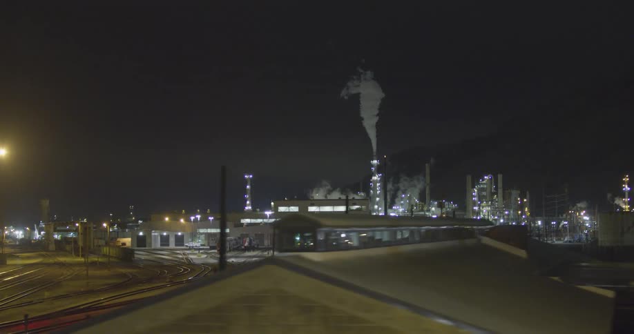 A landscape view of industrial area and train tracks with smoke billowing out of it