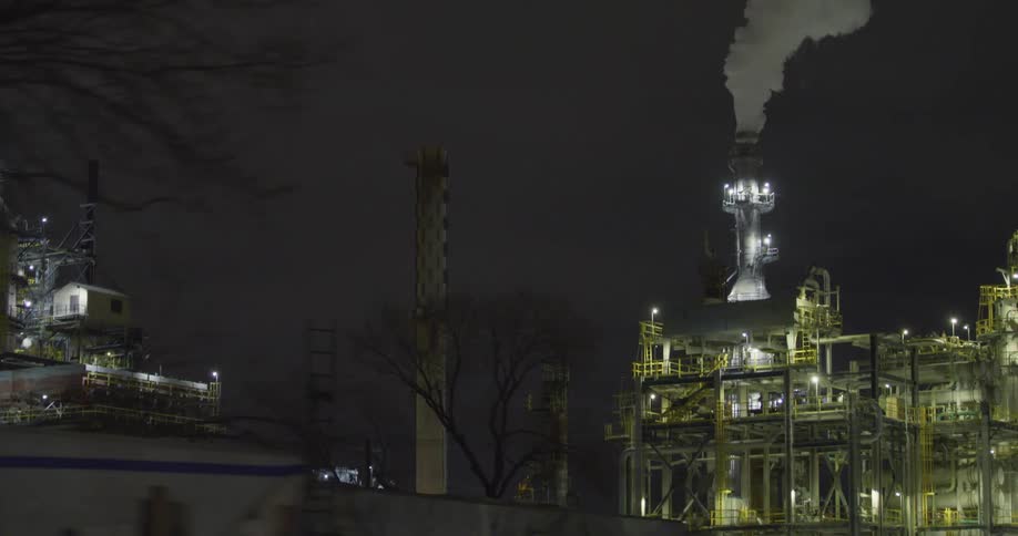 White clouds of steam and vapor rising from an oil refinery at night