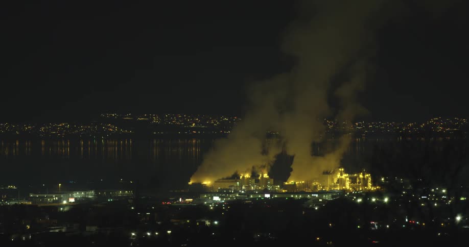 Pollution rising from a factory in a city at night