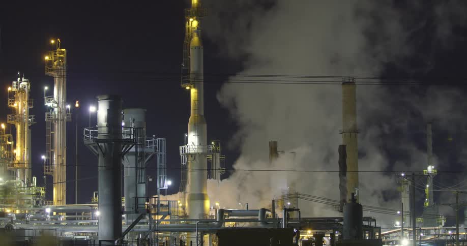 Clouds of steam and vapor rising from an oil refinery at night