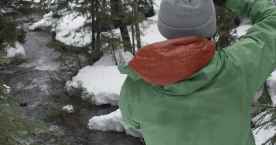 A man in a green jacket takes pictures of a snowy river