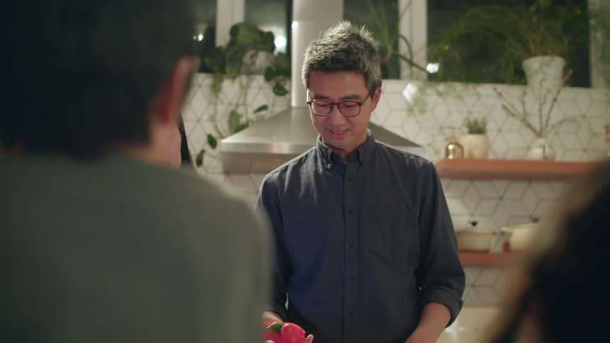 A man at home picks up a cut red pepper and shows it to his friends