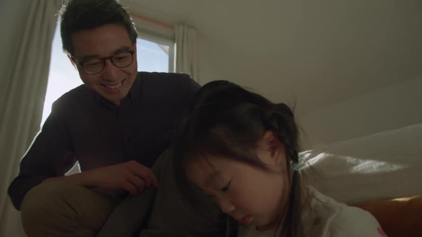 A man a boy and a girl in a bedroom looking at a tablet with a window in the background
