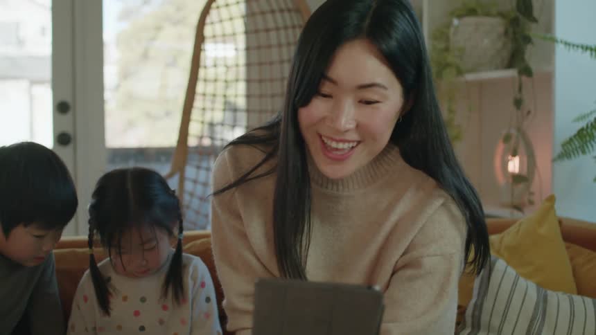 A woman sitting on the couch with her children talking on a tablet