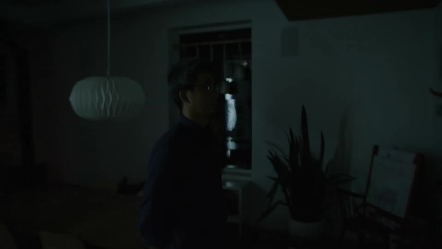 A man stands in his dark home as lights flash and cause shadows in the room