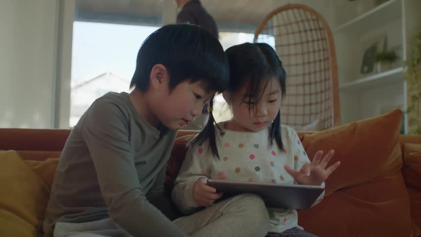 Two children playing on a tablet on a couch
