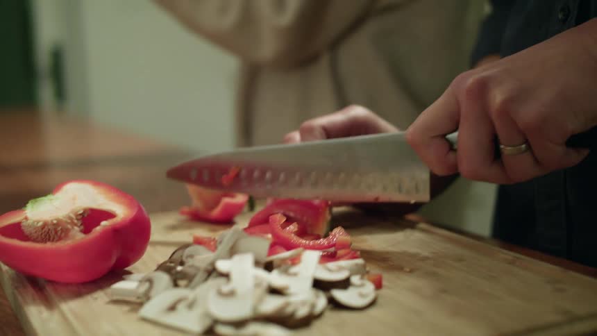 A man chops vegetables at home and his wife stands next to him