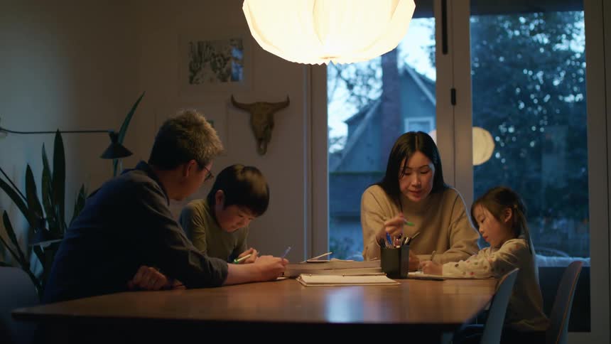 A man and woman sit at a table and help their children with school work