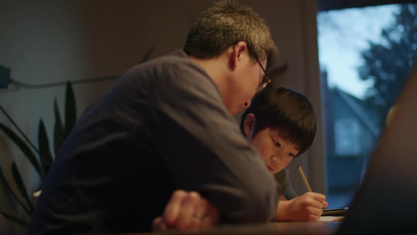 Father helping his son with homework on the dinning table at home